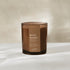 A beach bonfire scented candle in a translucent amber glass jar with a brown paper label, set against a warm beige background.