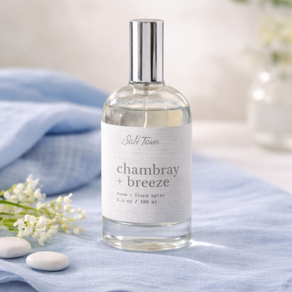 Bottle of Salt Town chambray + breeze room spray on a blue fabric background with white flowers.