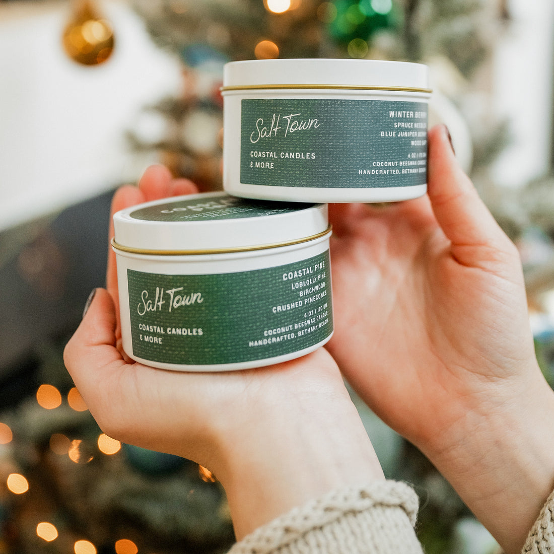 Two candles from Salt Town held by a person against a blurred festive background