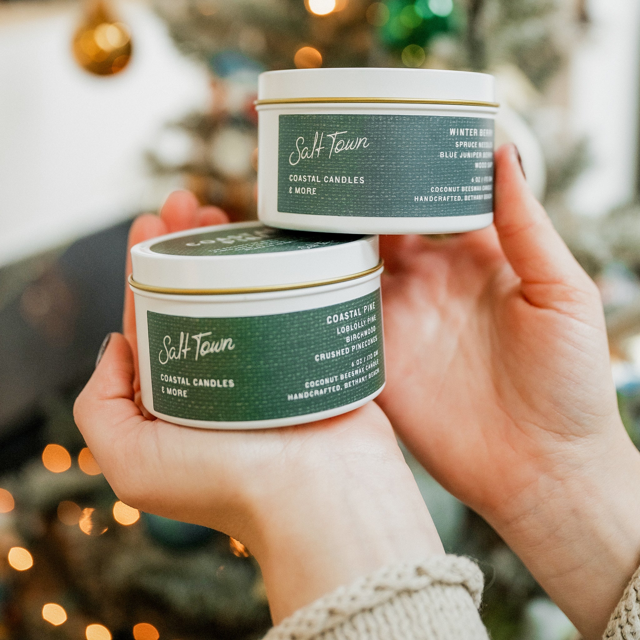 Two candles from Salt Town held by a person against a blurred festive background