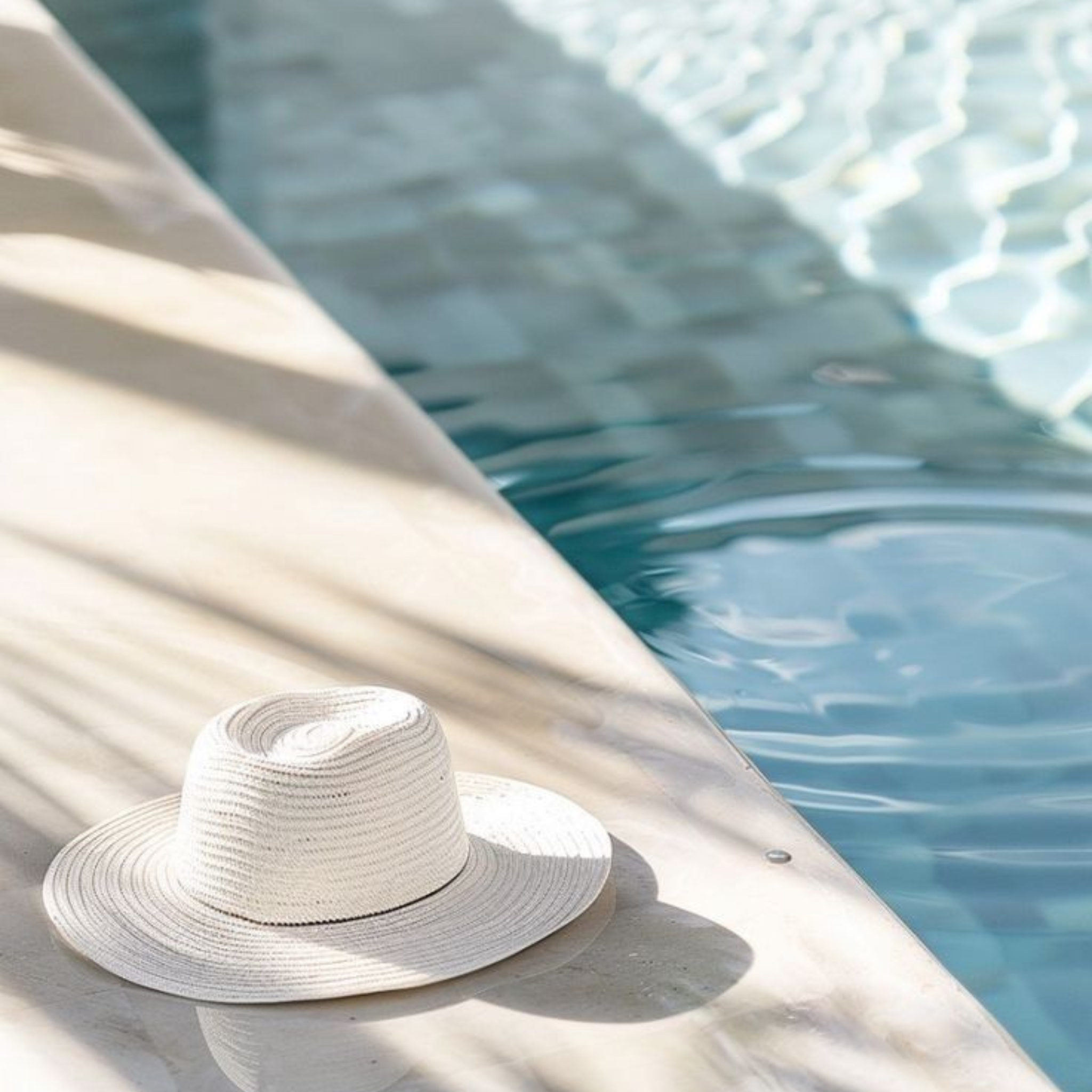 White straw hat on a poolside ledge with water in the background