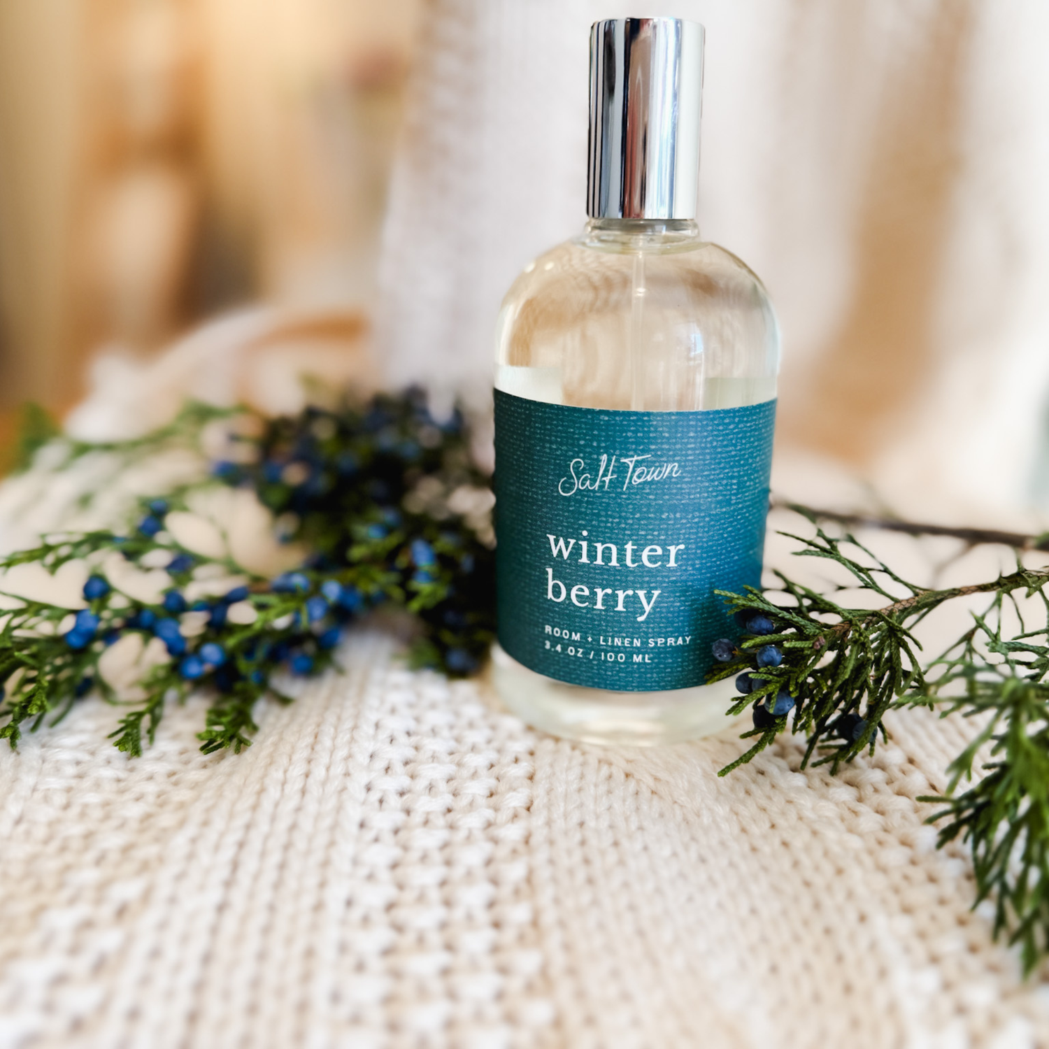 Image of glass room spray bottle on a knitted surface with juniper berries. 