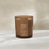 An amber glass jar candle with a brown paper label reading &